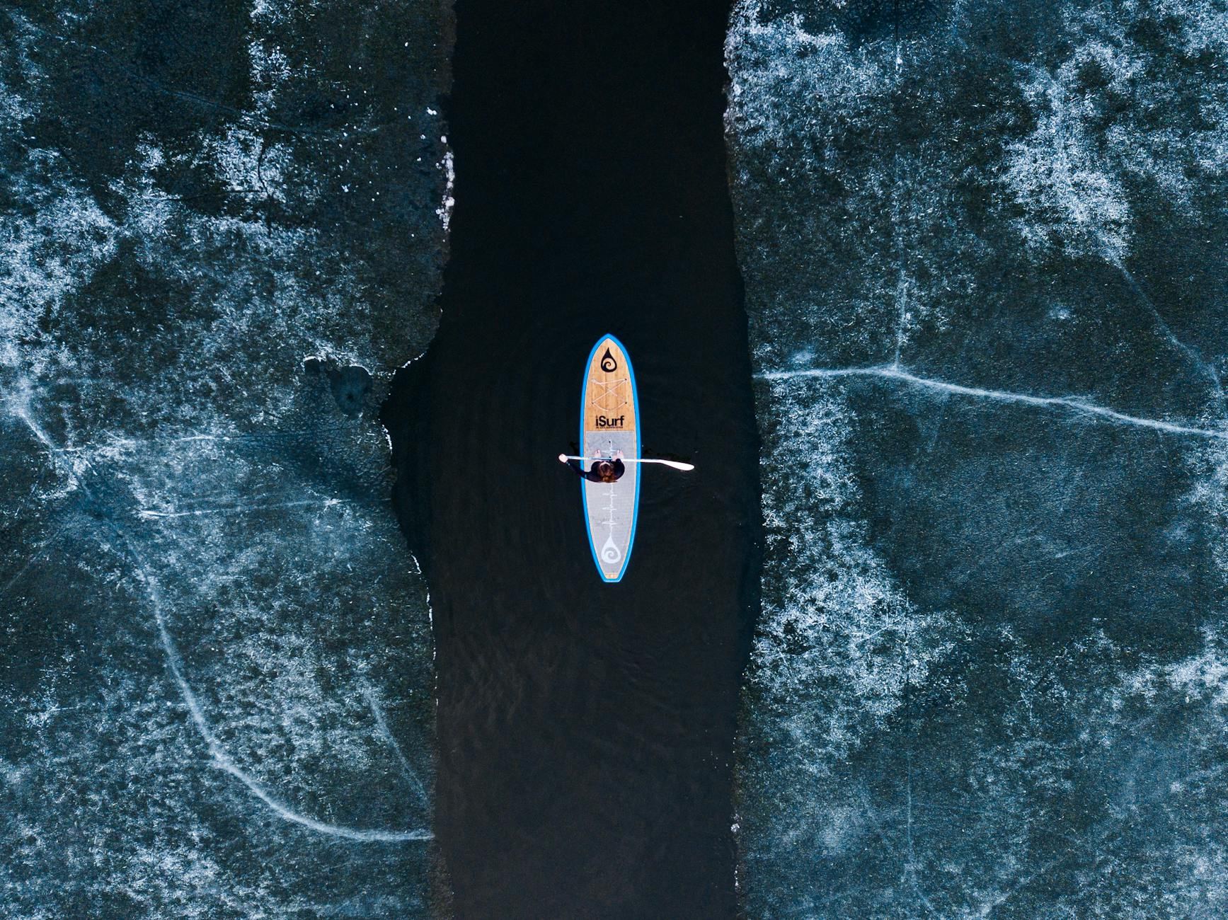 A lone paddleboarder glides across the icy blue waters of a Minnesota lake, framed by a winter landscape.