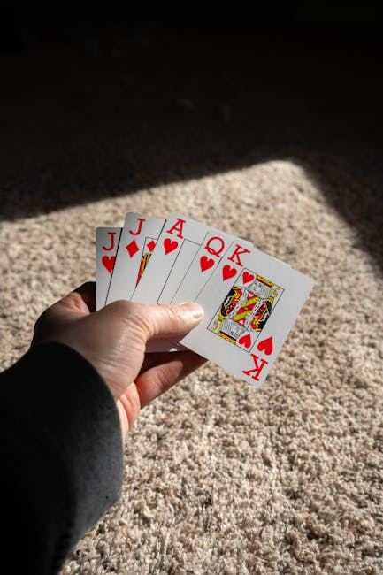 A hand holding a winning Euchre card hand with J, Q, K, and A of hearts.
