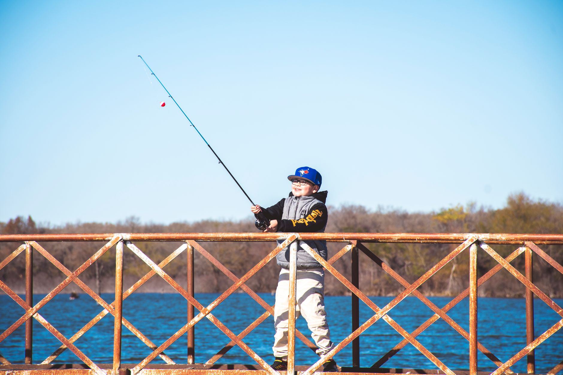 A young boy casts his line from a rustic pier, enjoying a sunny day amidst serene waters and lush greenery.