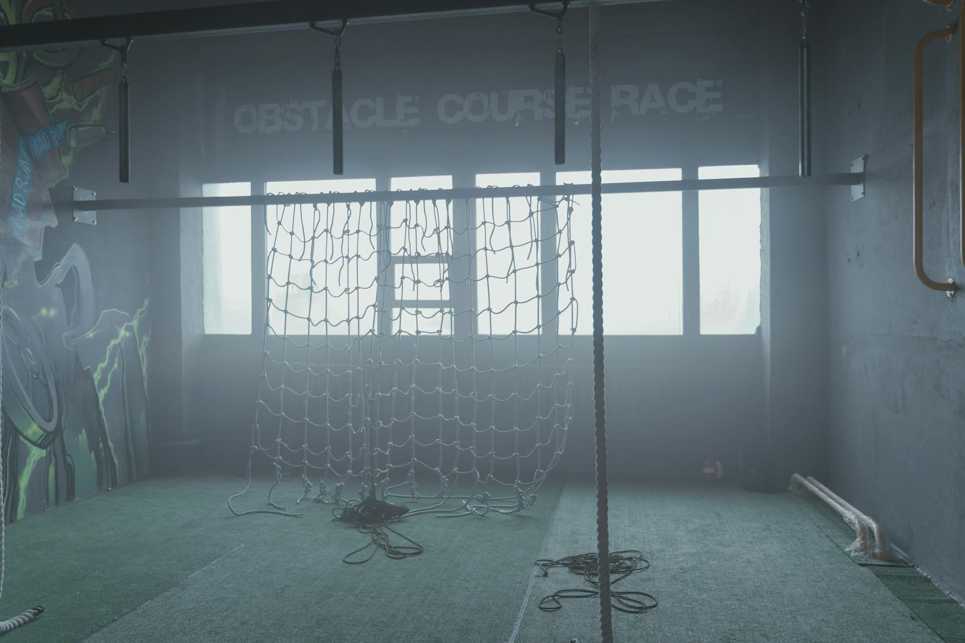 An indoor ninja gym showcasing a cargo net and climbing ropes designed for obstacle course training.