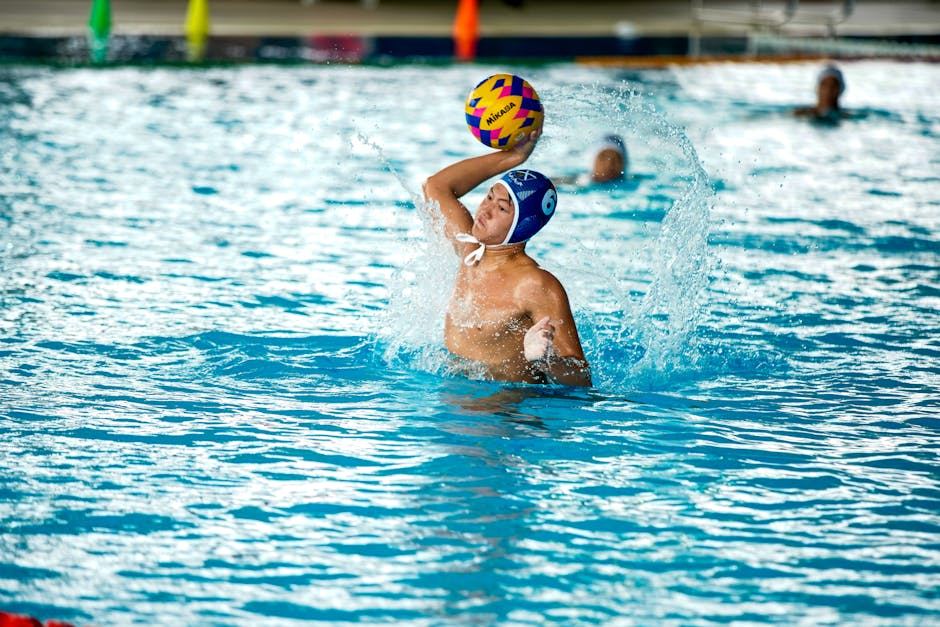 A male water polo player prepares to throw a ball while swimming in a pool.