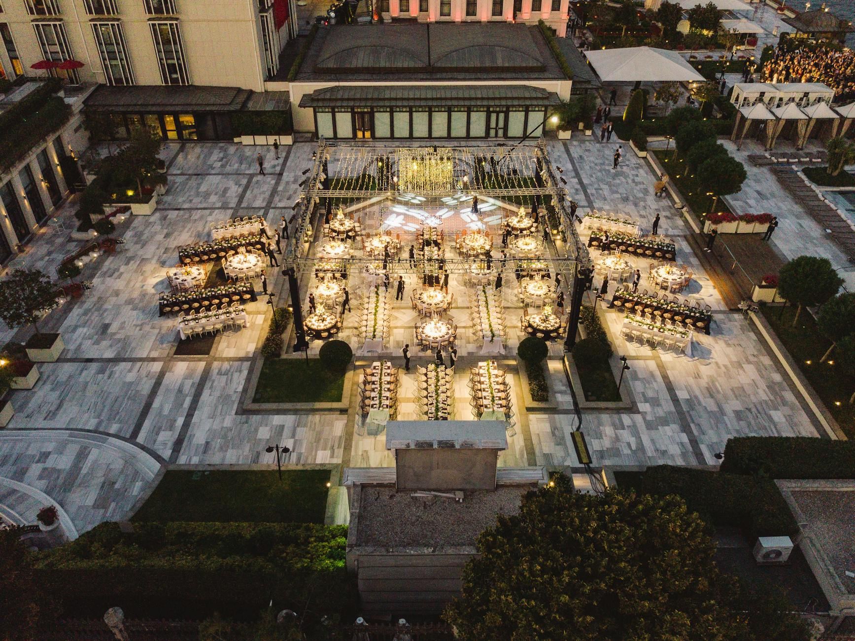 A beautifully lit outdoor evening event in a luxurious urban courtyard, featuring elegant table settings.