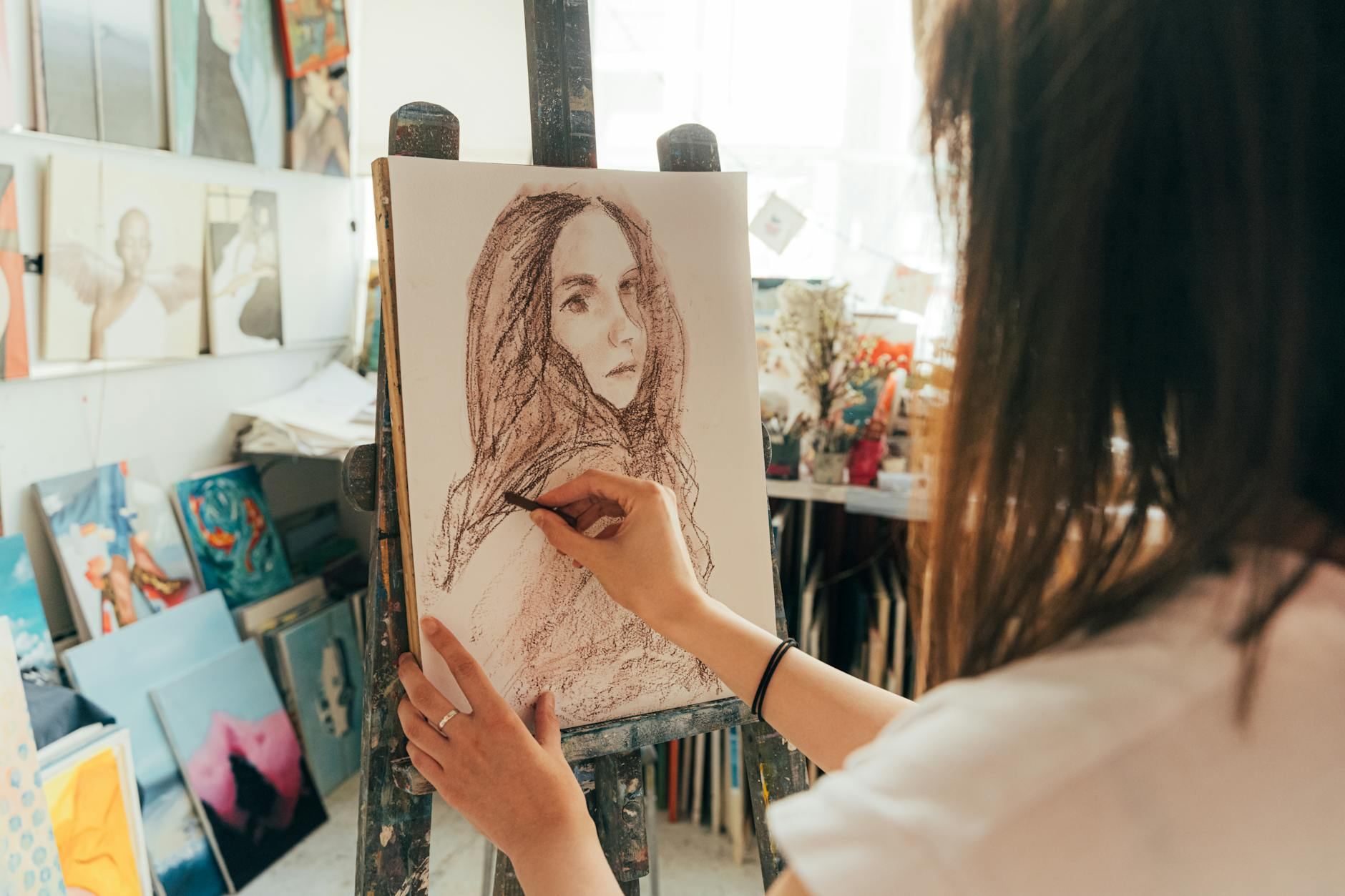 An artist skillfully draws a portrait using charcoal in a bright art studio, showcasing creativity and focus.