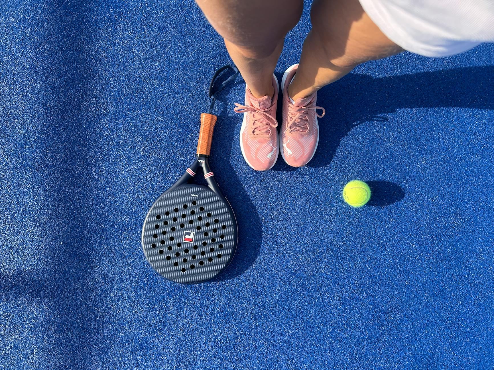 Top view of a padel player with shoes, racket, and ball on a vibrant blue court.