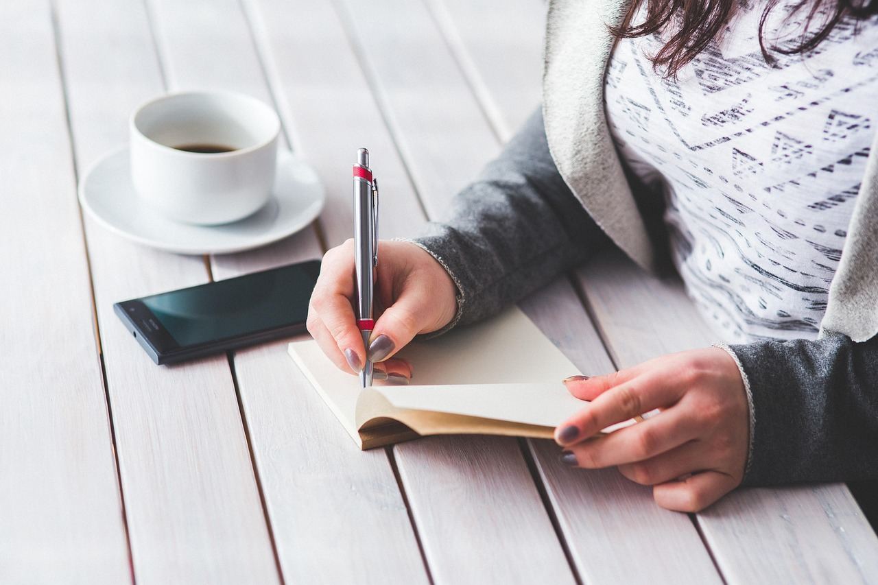 A person writes in a notebook with a pen, reflecting on the topic 'Is Essay Writing for you? Let's find out!'