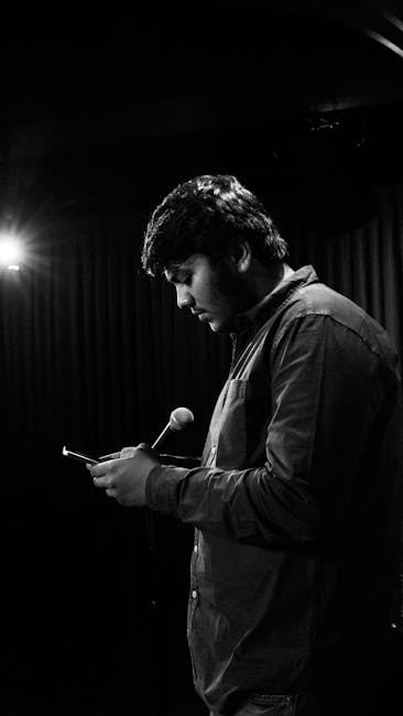 A comedian performing on stage, holding a phone and microphone, deep in thought.