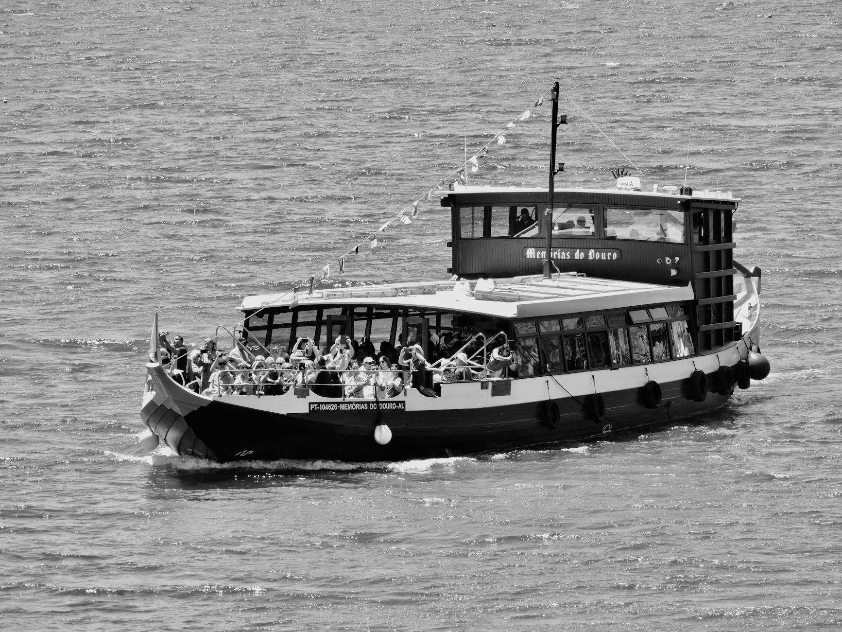 A vintage black and white scene captures a crowded tour boat gliding along the scenic Douro River.
