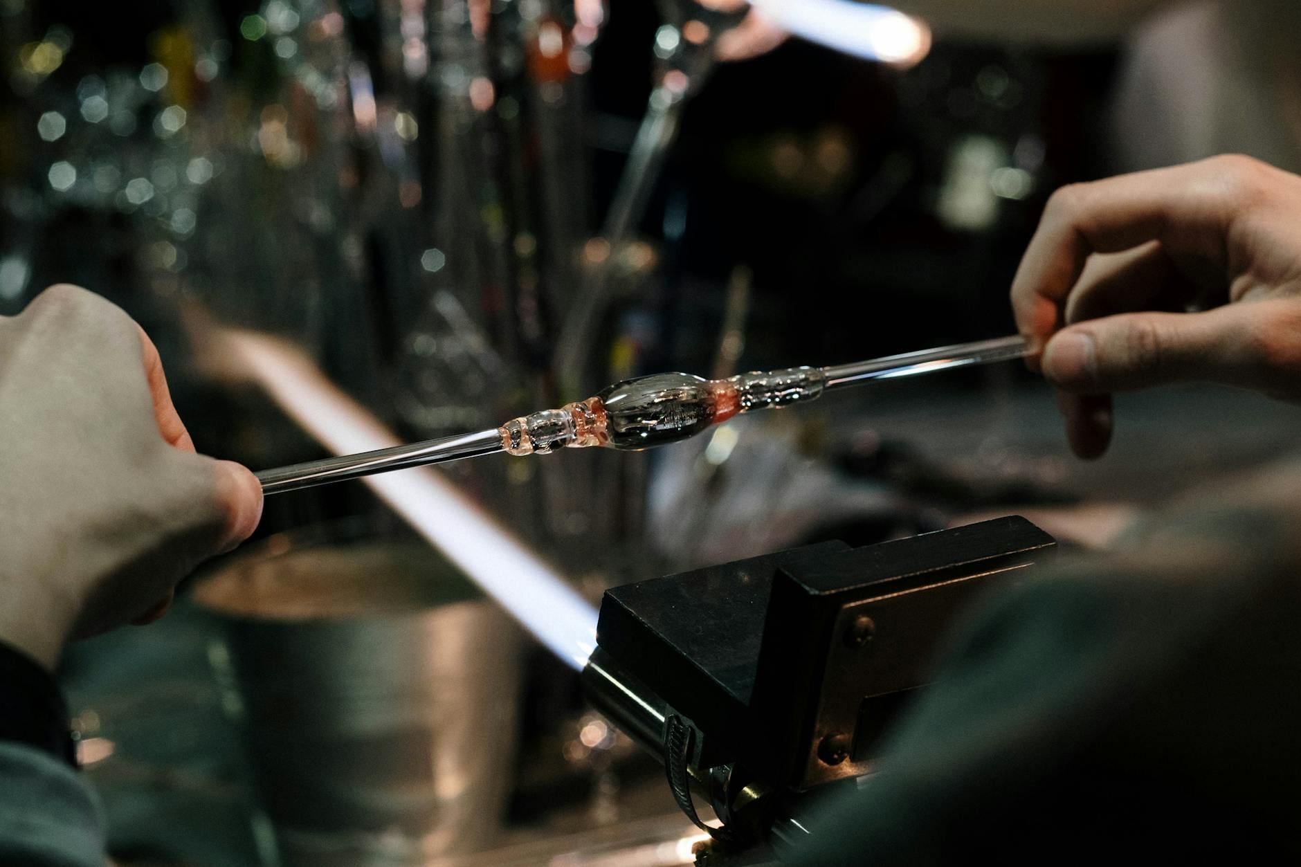 A skilled craftsman expertly shapes molten glass with precision in a vibrant ceramics and glassblowing workshop.