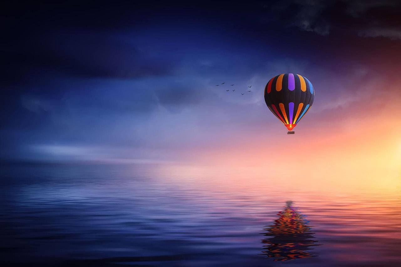A colorful hot air balloon floats over a tranquil water surface at sunrise. Is Hot Air Ballooning for you? Let's find ou