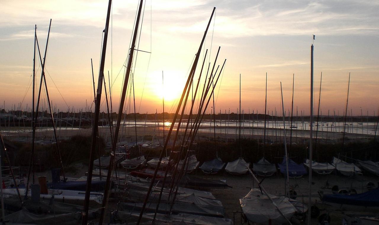 A panoramic view of Hayling Island's tranquil waters, dotted with colorful sailboats gliding gracefully under a clear blue sky.