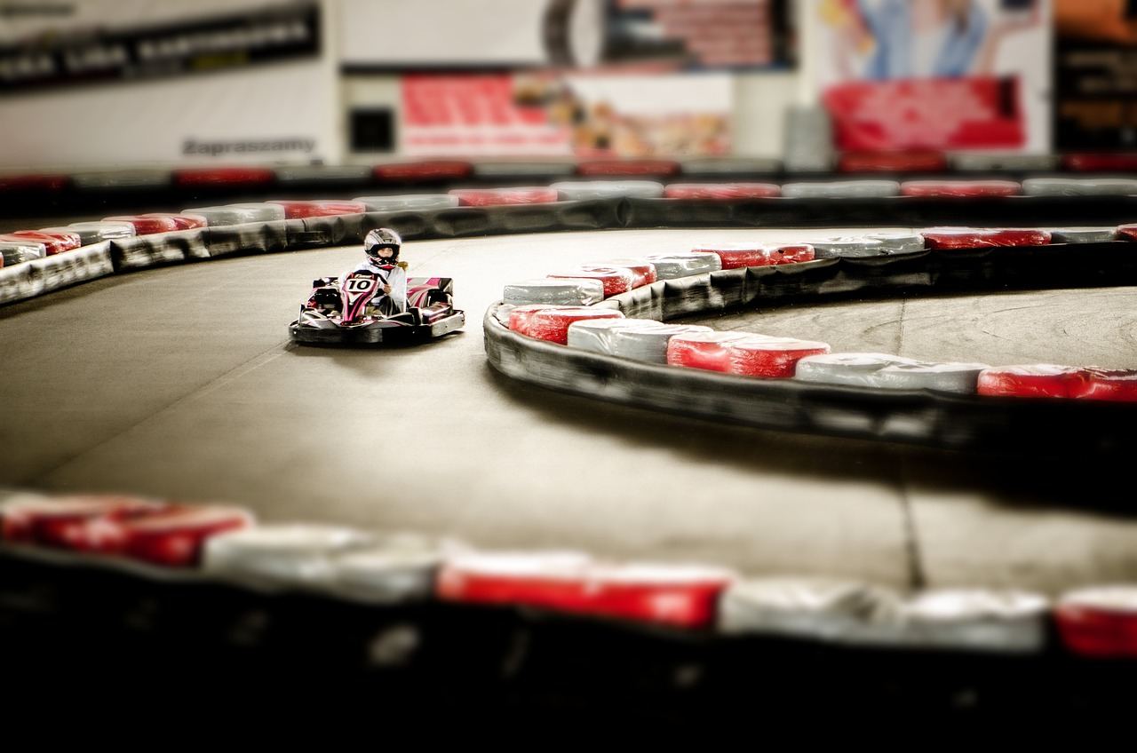 A vibrant go-kart track featuring colorful karts racing around a winding circuit under a clear blue sky.