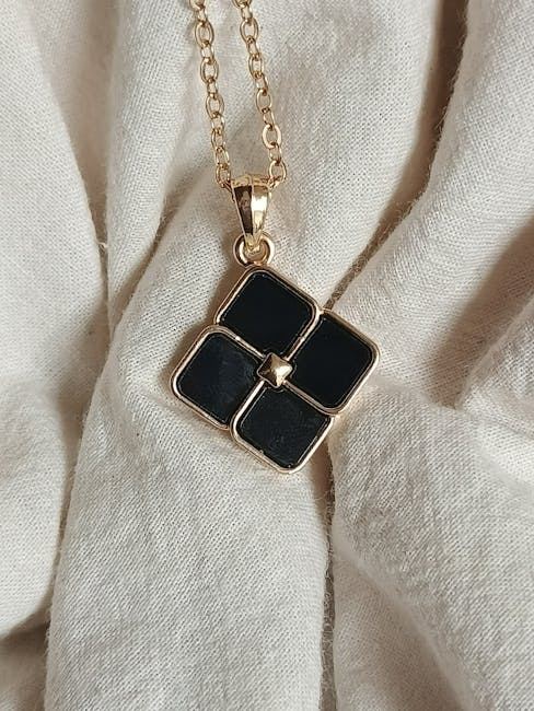 A gold necklace featuring a black pendant in a floral design, resting on a light fabric.