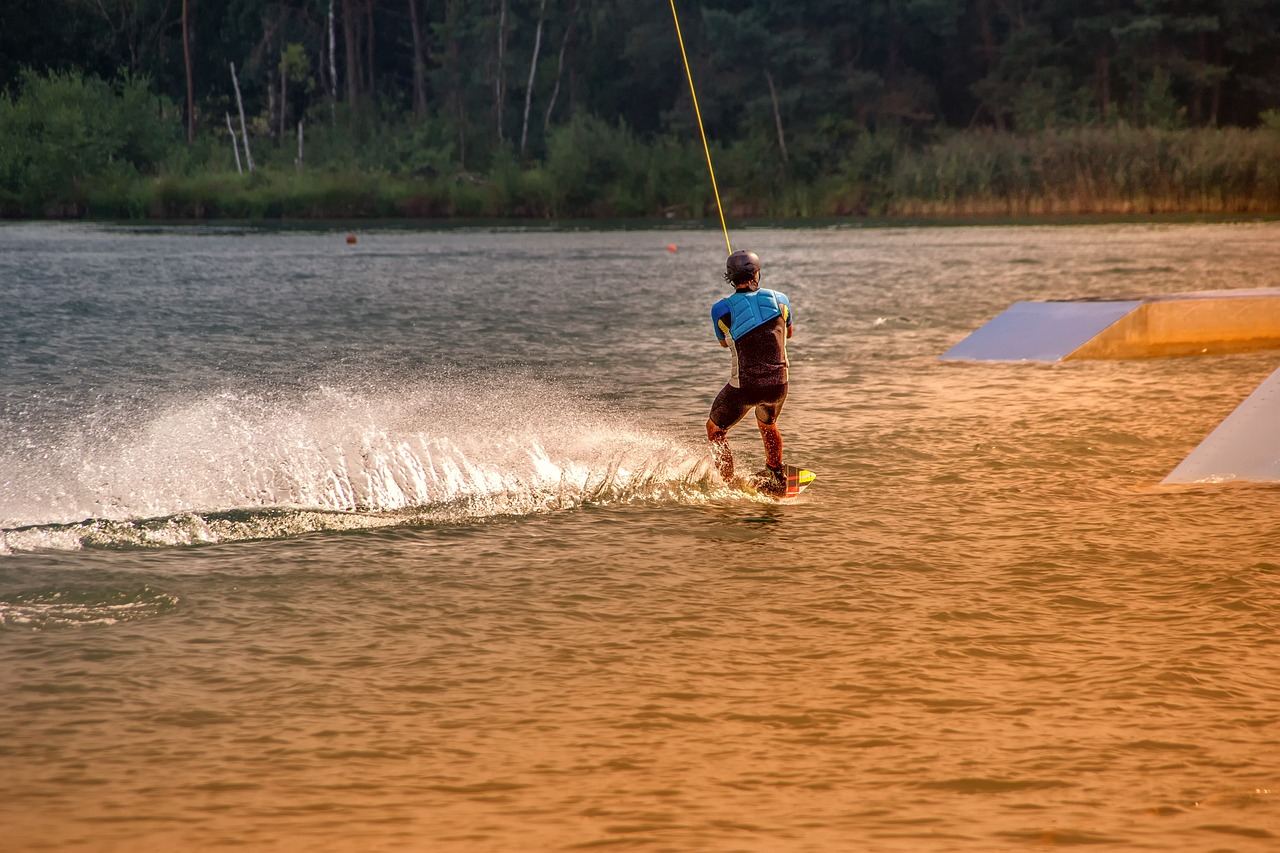 A wakeboarder glides across the shimmering water, expertly carving through the waves with a backdrop of a clear blue sky.