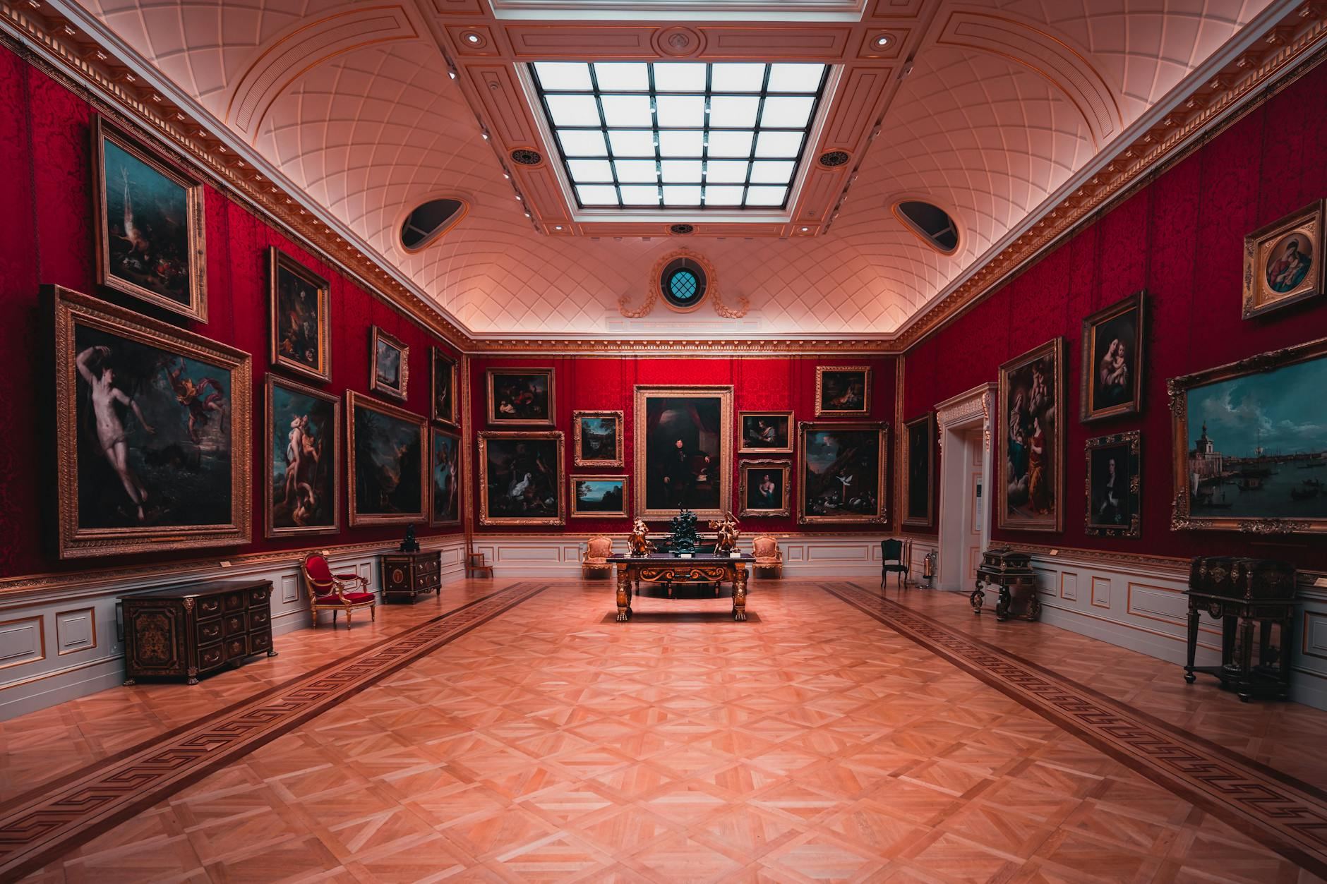 Explore the grandeur of an art gallery room in London with elegant red walls and classic paintings.