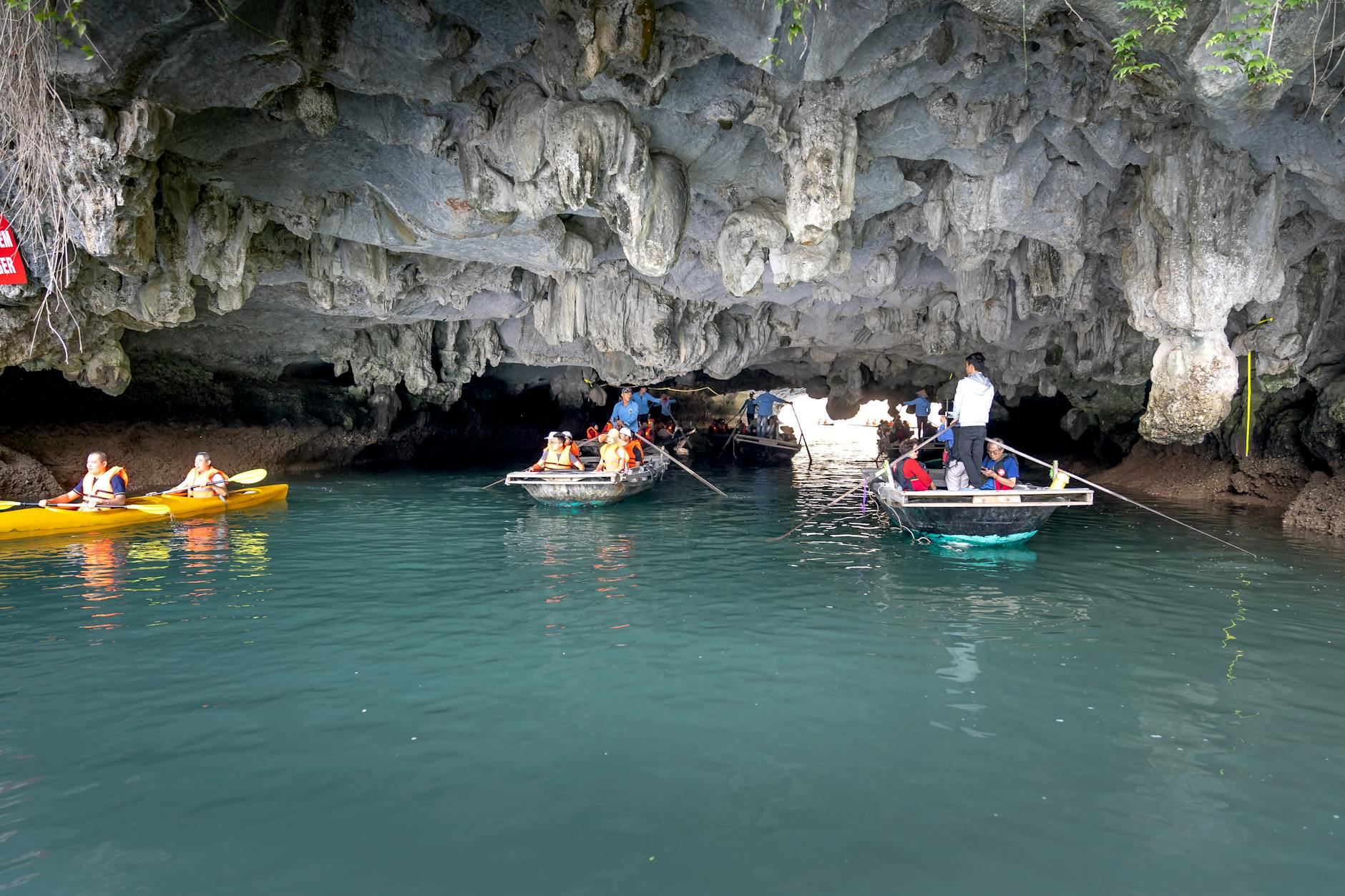 Tourists navigate through tranquil waters, marveling at breathtaking cave formations while kayaking and boating.