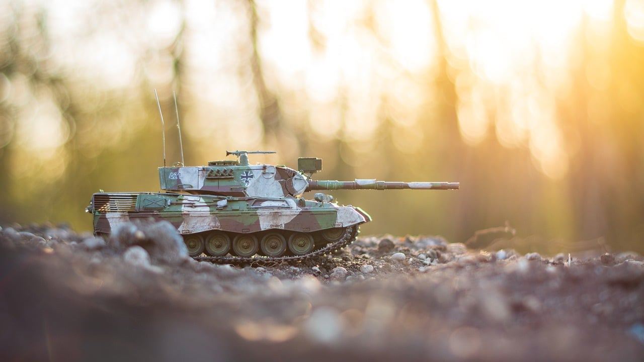 A detailed miniature model of a Leopard 1 tank positioned on a textured battlefield, ready for wargaming.