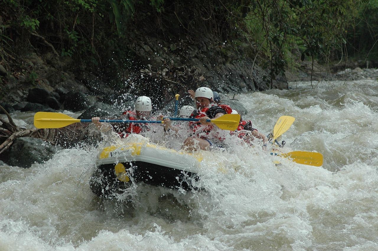 A group of adventurous rafters navigates a turbulent river, splashing through waves and surrounded by lush greenery.