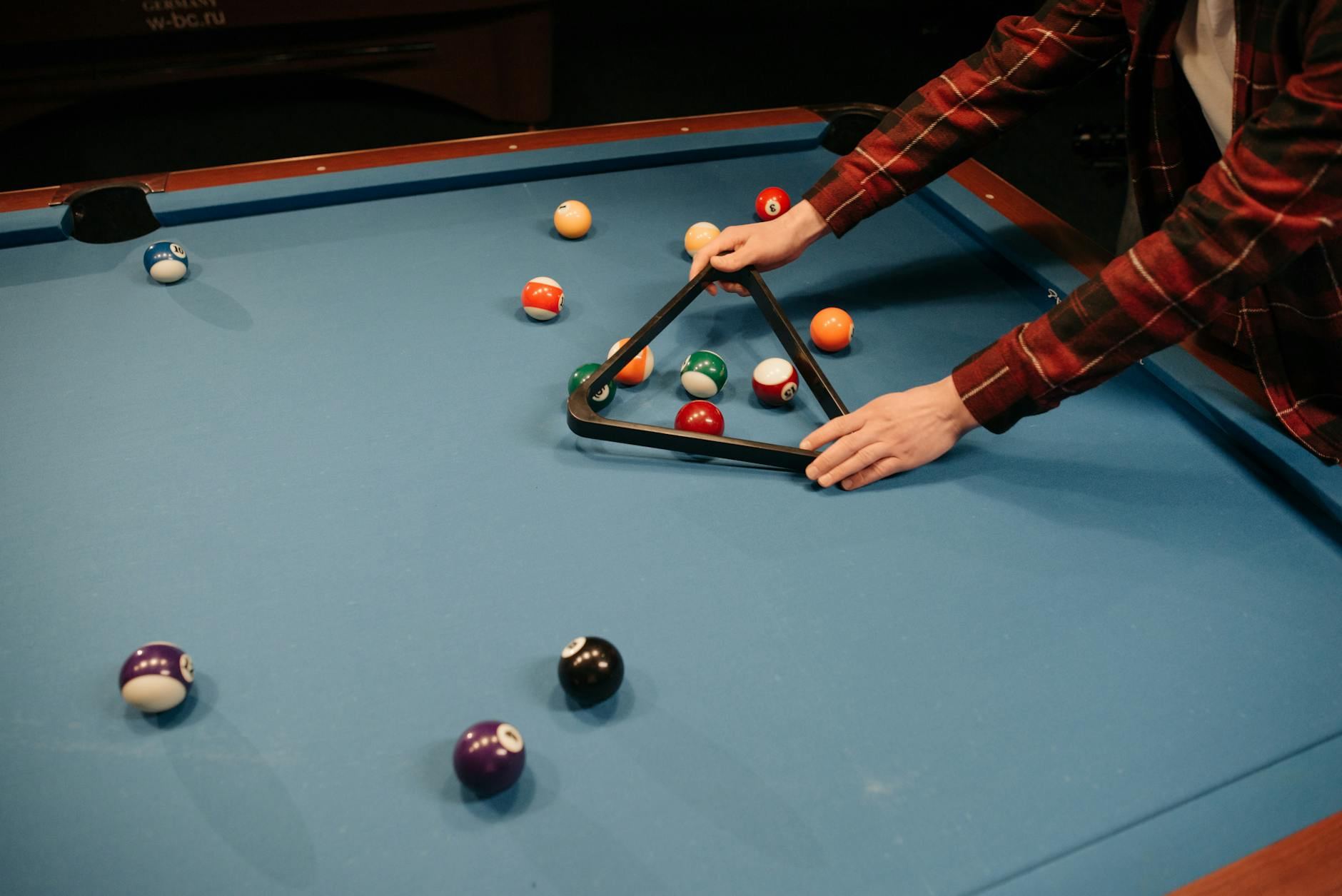 A player meticulously arranges colorful billiard balls in a triangle on a vibrant blue pool table, ready for a game.