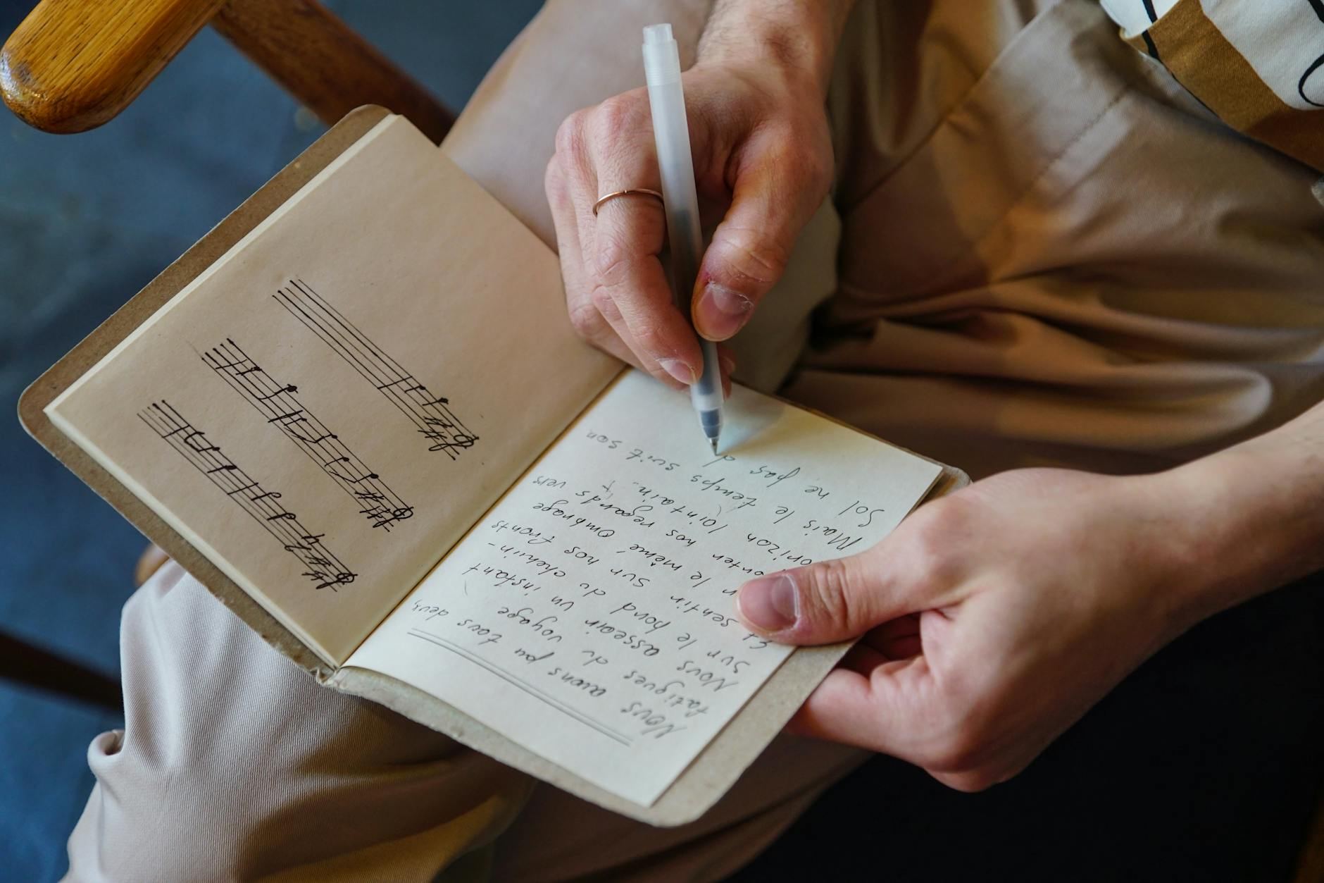 Male songwriter writes lyrics and music notes in a notebook, capturing the creative process.