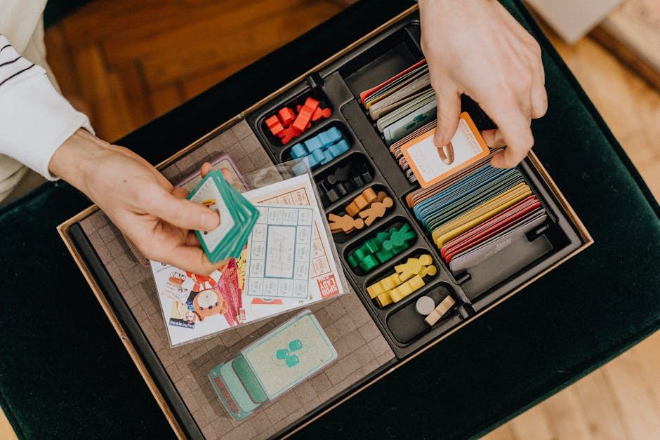 A person’s hands are shown arranging cards and game pieces from the Dominion board game. The game box is open, revealing colorful cards, wooden tokens, and various game components neatly organized in compartments. The background features a wooden floor, adding warmth to the scene.