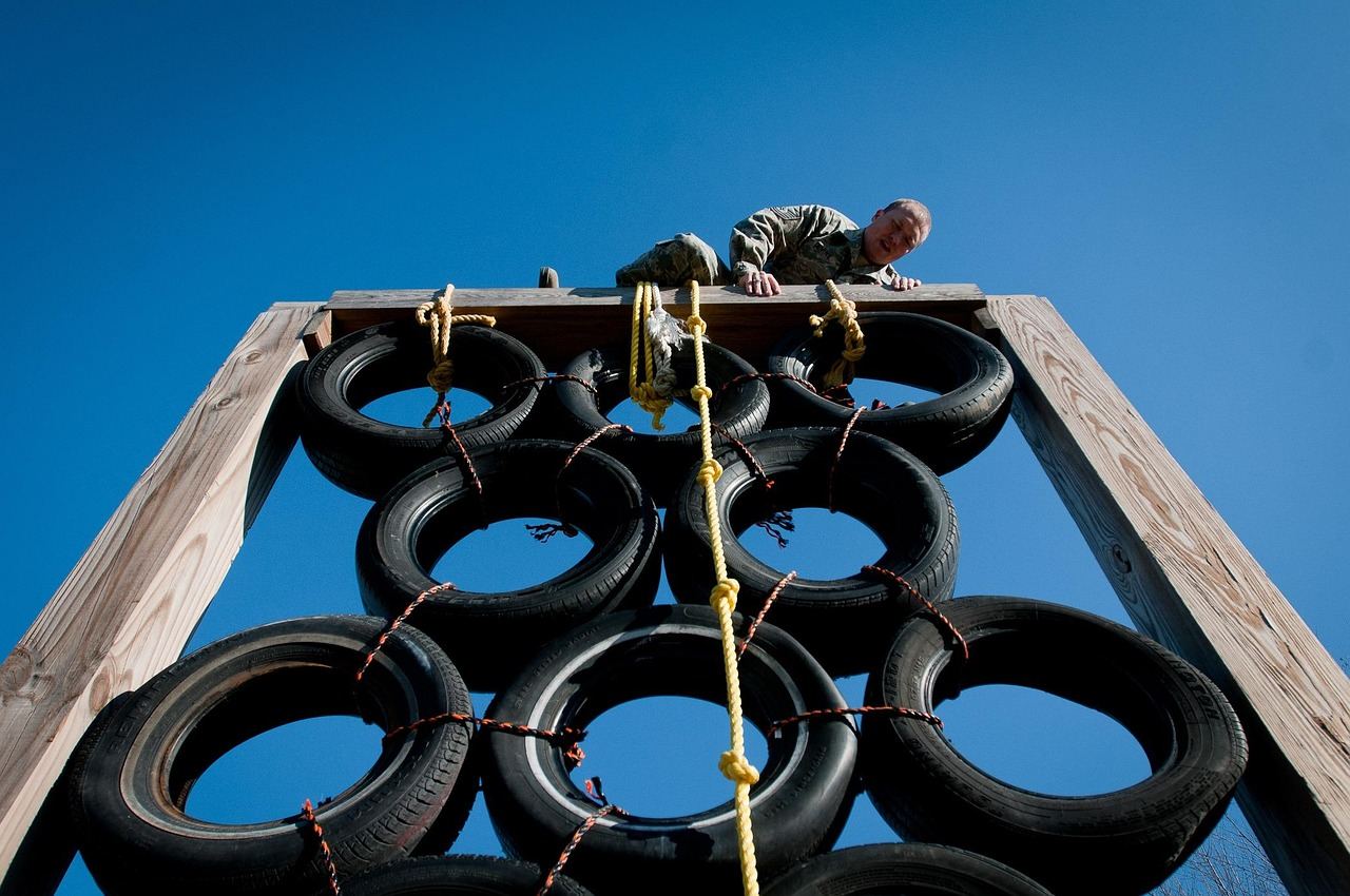 A determined man navigates a challenging outdoor obstacle course, climbing over barriers and swinging across ropes.
