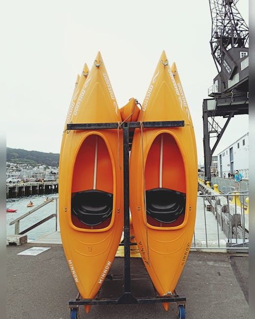 Two orange kayaks stacked on a rack by the water, ready for sprint kayaking.