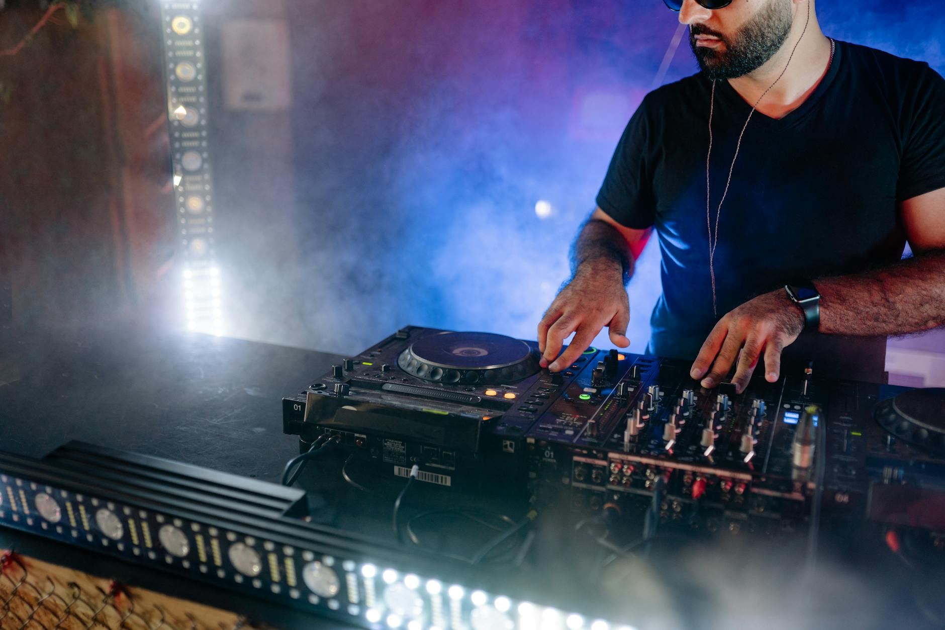 Energetic DJ performing live with mixing equipment in a colorful nightclub setting.