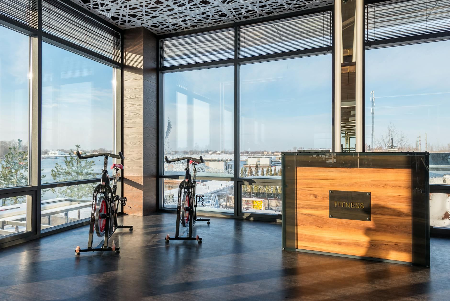 Bright and airy spin studio featuring modern exercise bikes and a wooden reception desk, illuminated by sunlight through panoramic windows.