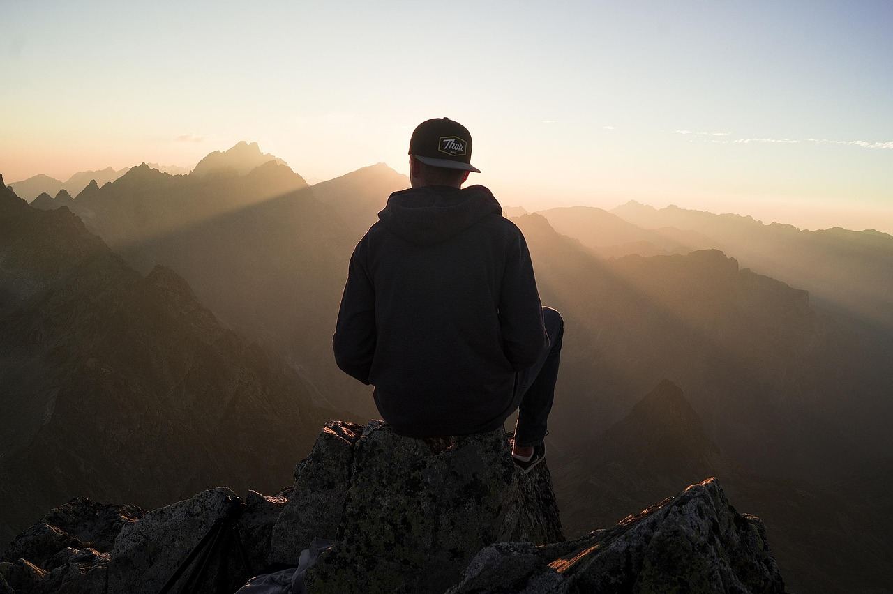A person sits on a mountain peak, contemplating nature, embodying the spirit of peak bagging.