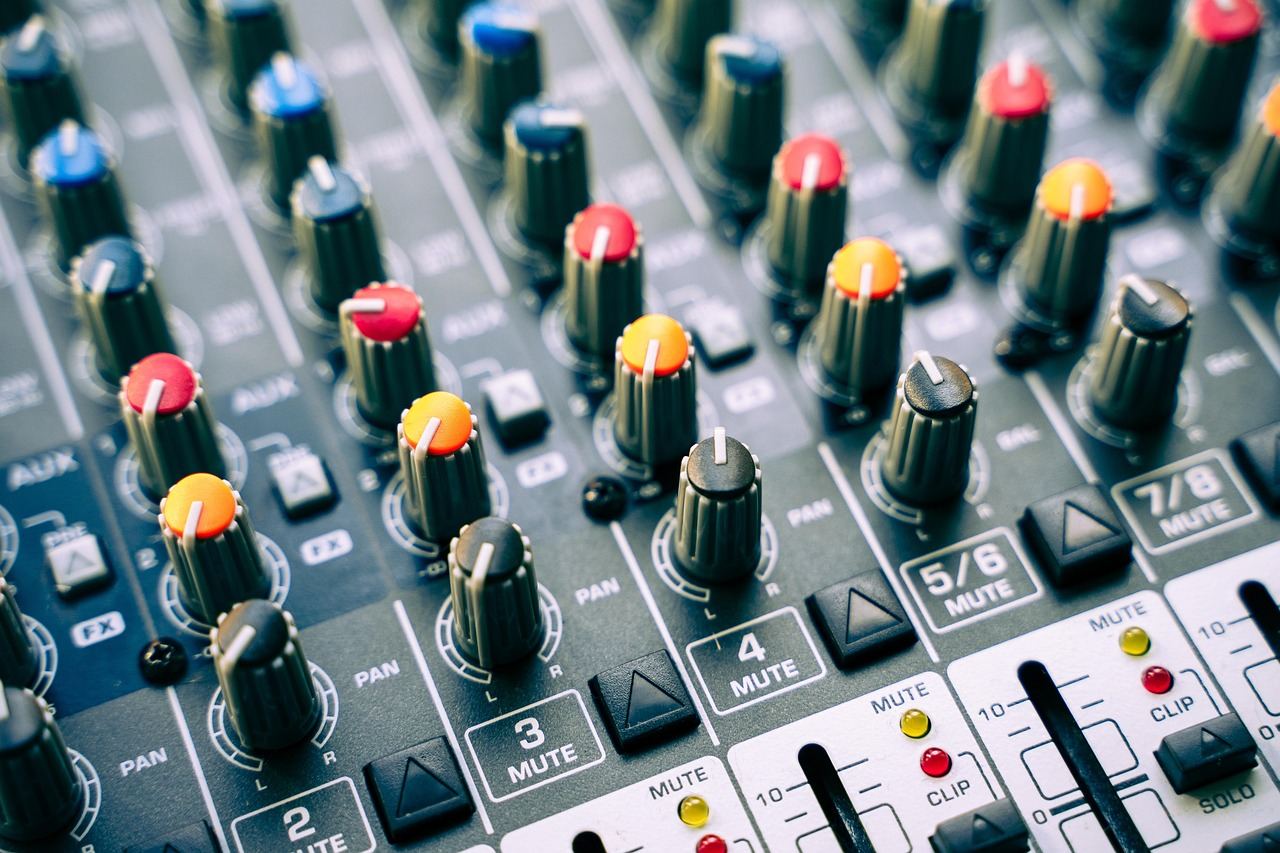 A professional audio mixer with colorful faders and knobs, set against a backdrop of sound equipment and cables.