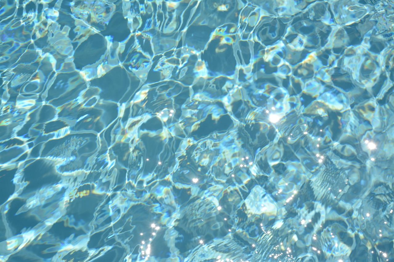 A sparkling blue swimming pool surrounded by lounge chairs and vibrant green plants under a clear blue sky.