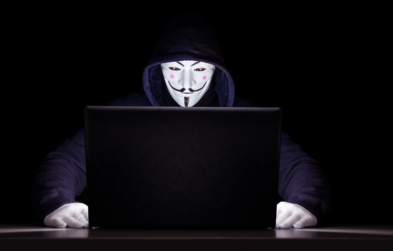 A hooded figure with a mask working on a laptop, representing the intrigue of cryptography.