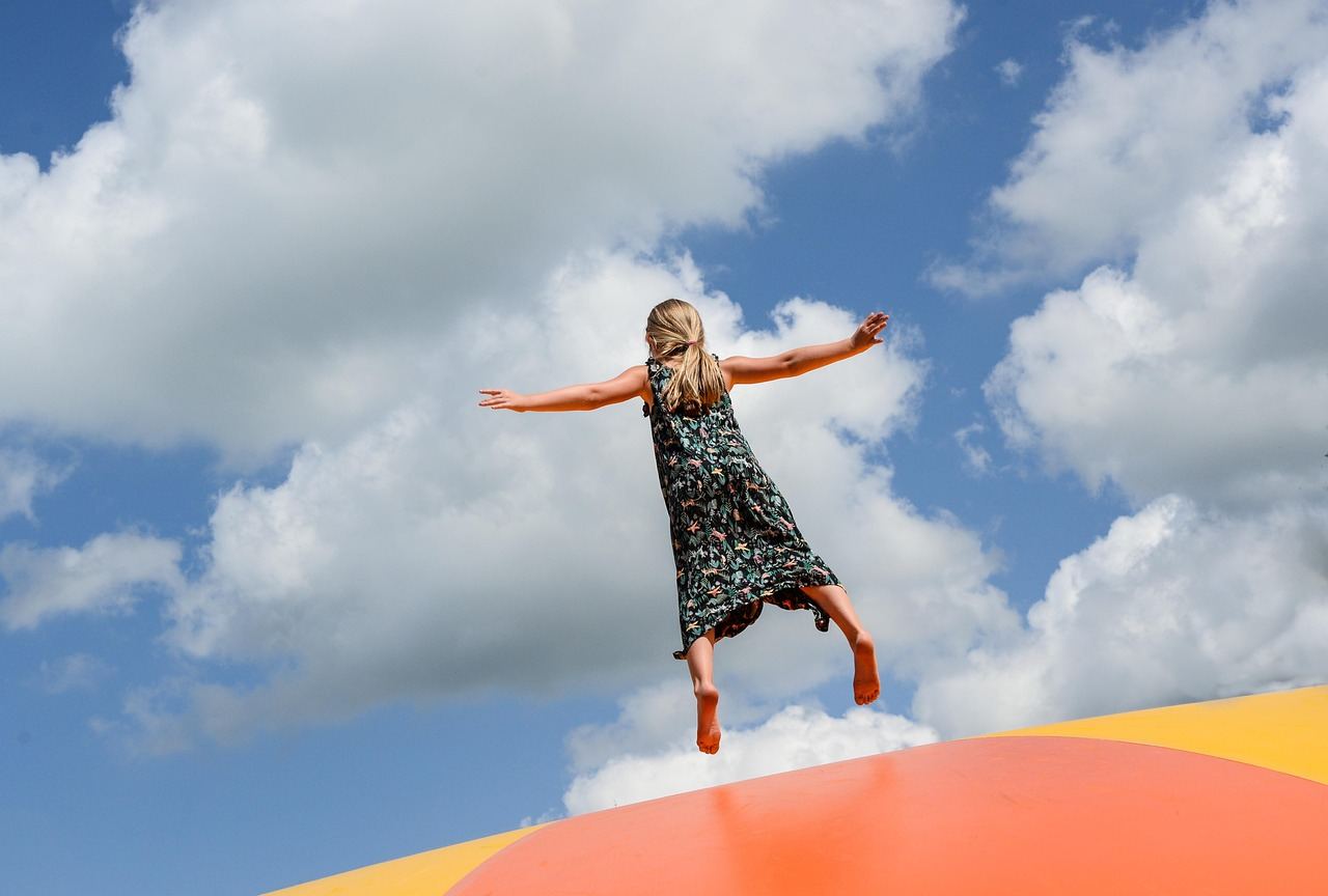 A young girl joyfully bouncing on a trampoline, surrounded by colorful mats and other children in a lively trampoline park.