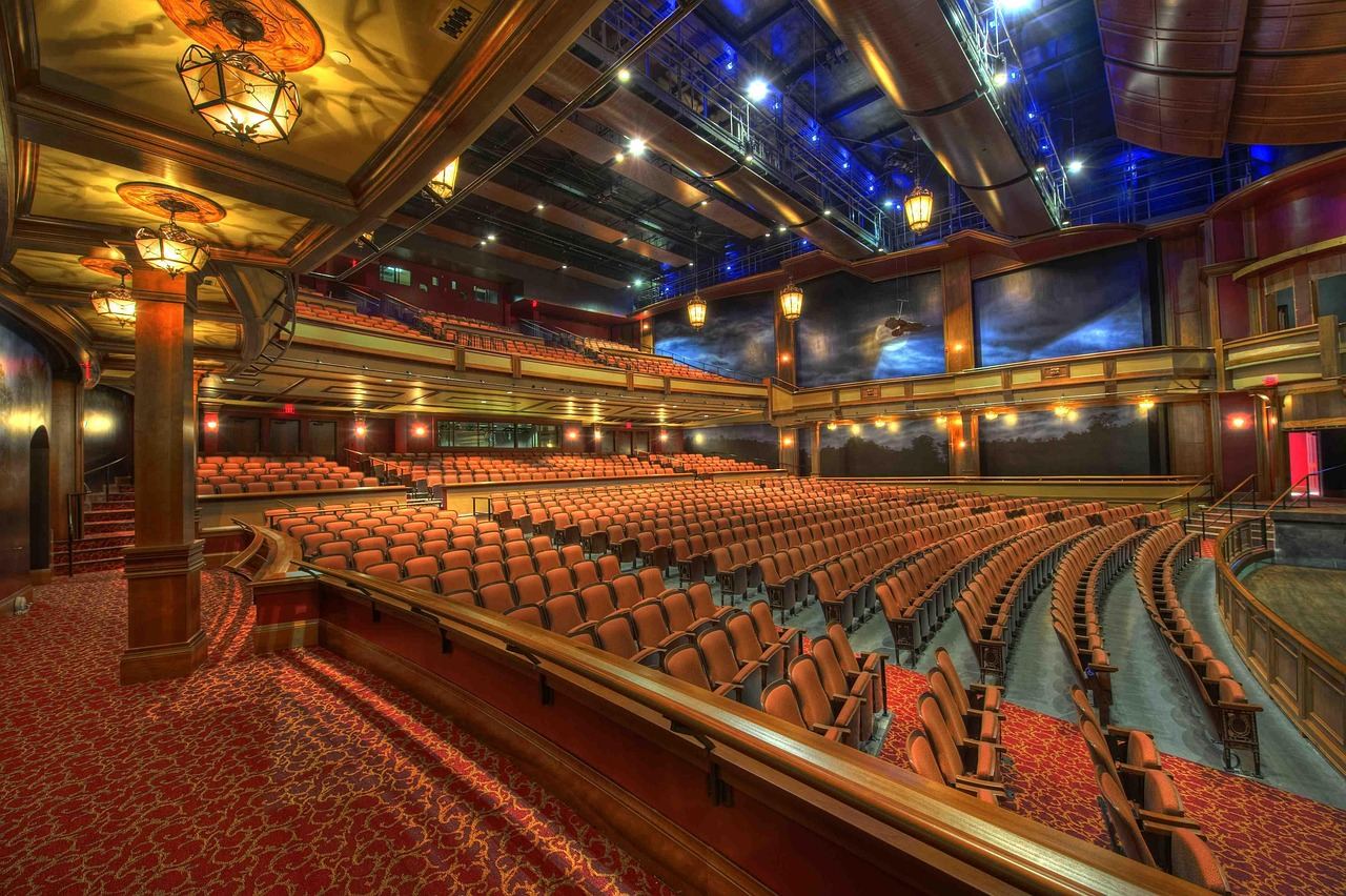 A grand auditorium featuring tiered seating, elegant chandeliers, and a large stage set for a performance.