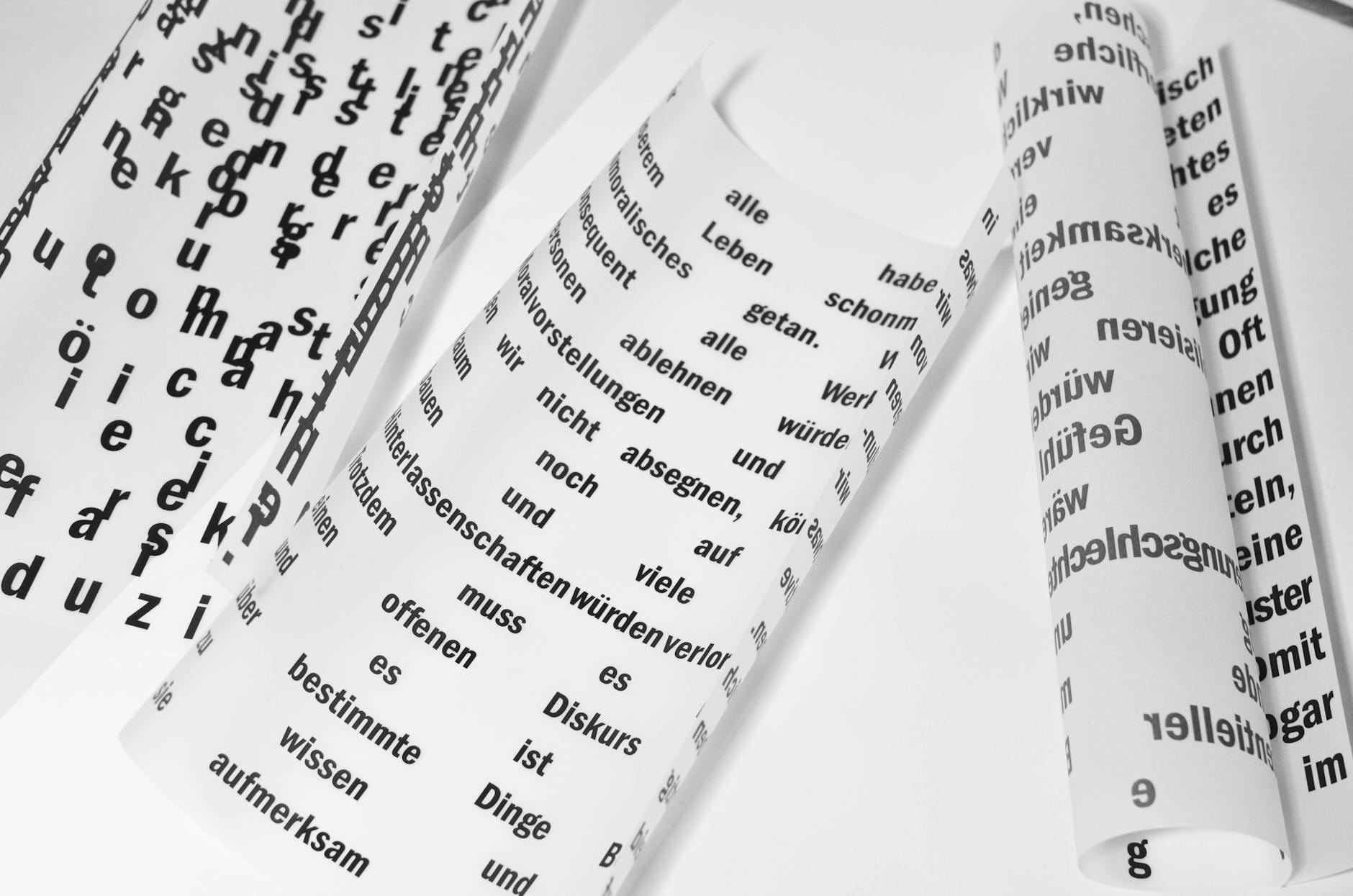 Rolled sheets of paper with German inscriptions are neatly arranged on a bright white surface, showcasing a creative workspace.