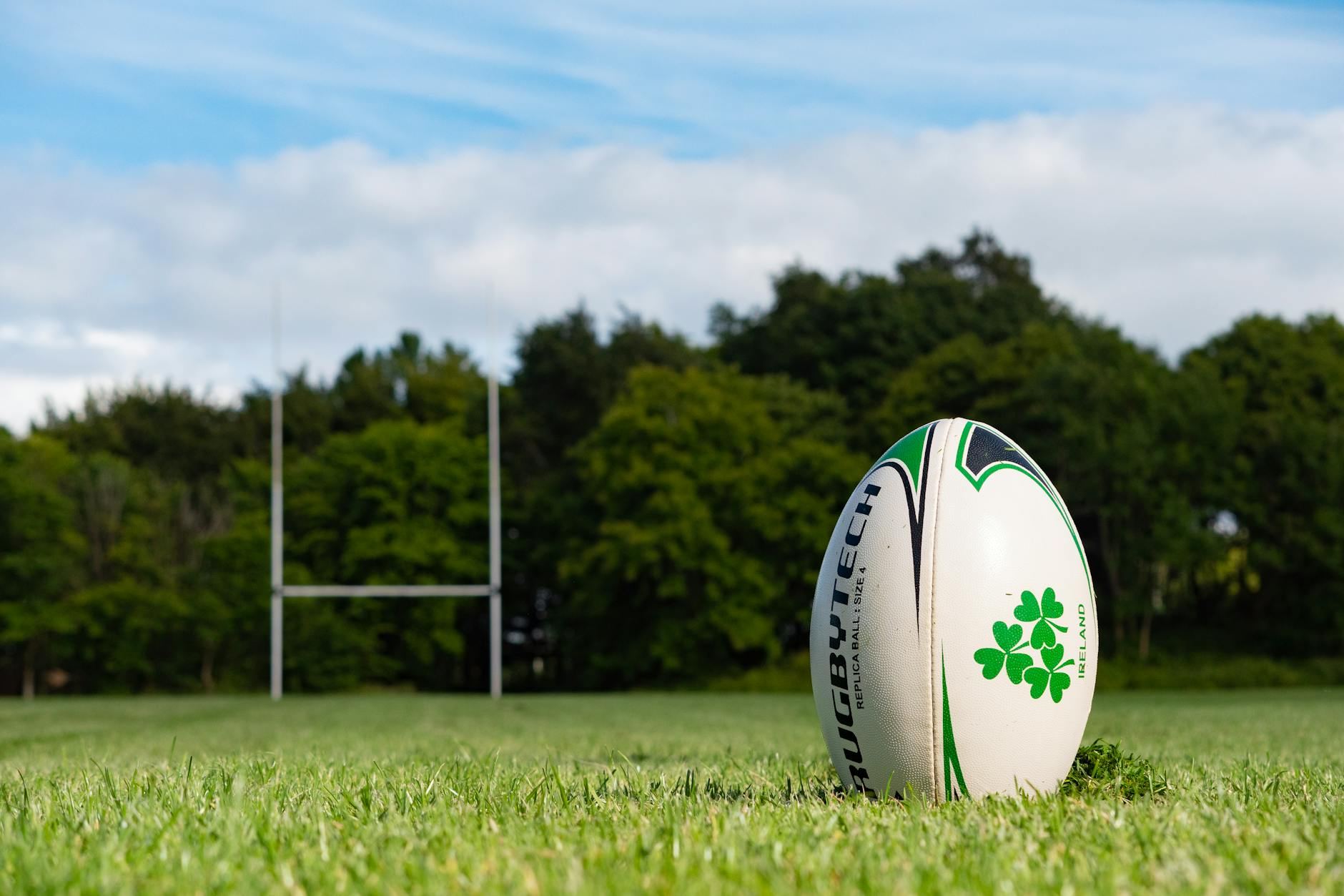 A rugby ball rests on a vibrant green pitch under the warm summer sun in Galway, Ireland.