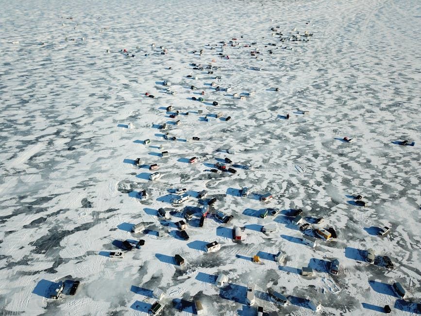 Aerial view of numerous ice fishing huts scattered across a frozen lake.