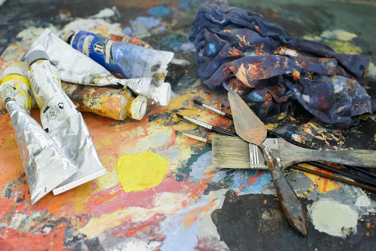 A focused artist stands in front of a canvas, brush in hand, surrounded by vibrant paints and tools.