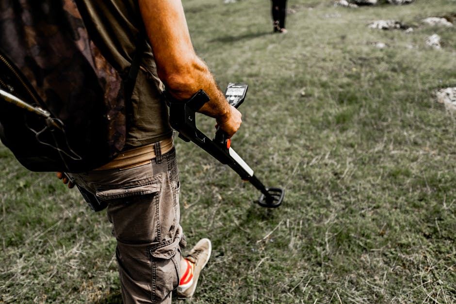 A person using a metal detector in a grassy area, exploring for potential finds.
