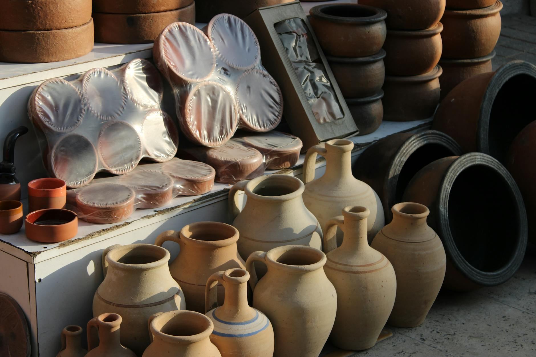 Colorful, handcrafted clay pottery pieces in various shapes and sizes are beautifully arranged at a vibrant outdoor market.