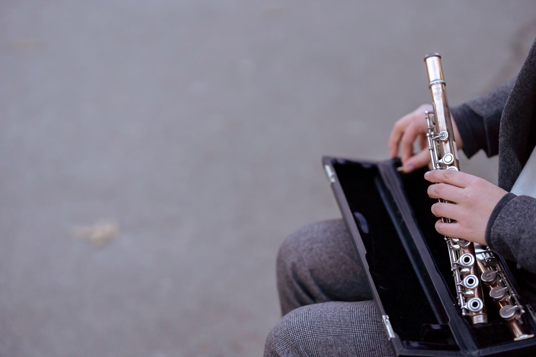 Hands holding a silver flute outdoors, highlighting musician's intimate connection with the instrument.