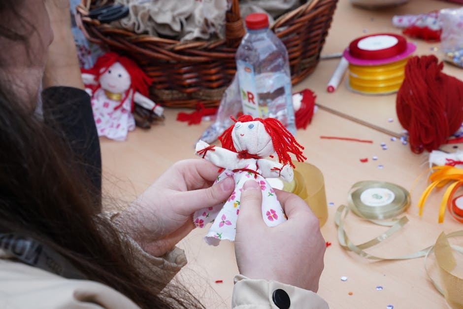 A person holding a handmade doll with red yarn hair, surrounded by crafting materials.