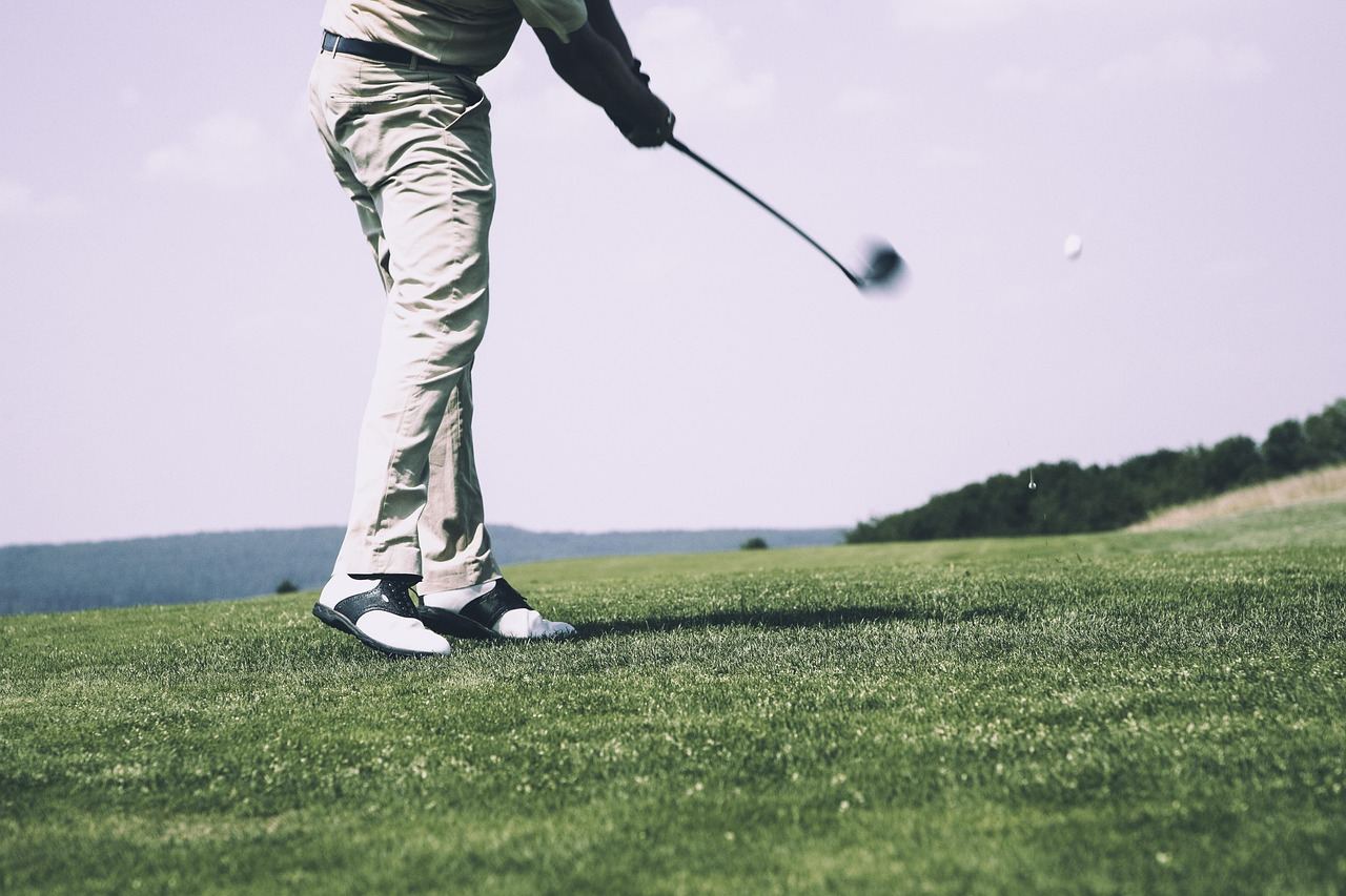 A serene golf course with lush green fairways, a clear blue sky, and a golfer preparing to tee off.