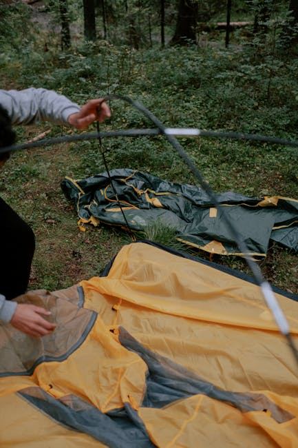 A person setting up a yellow and green tent in a forested area.