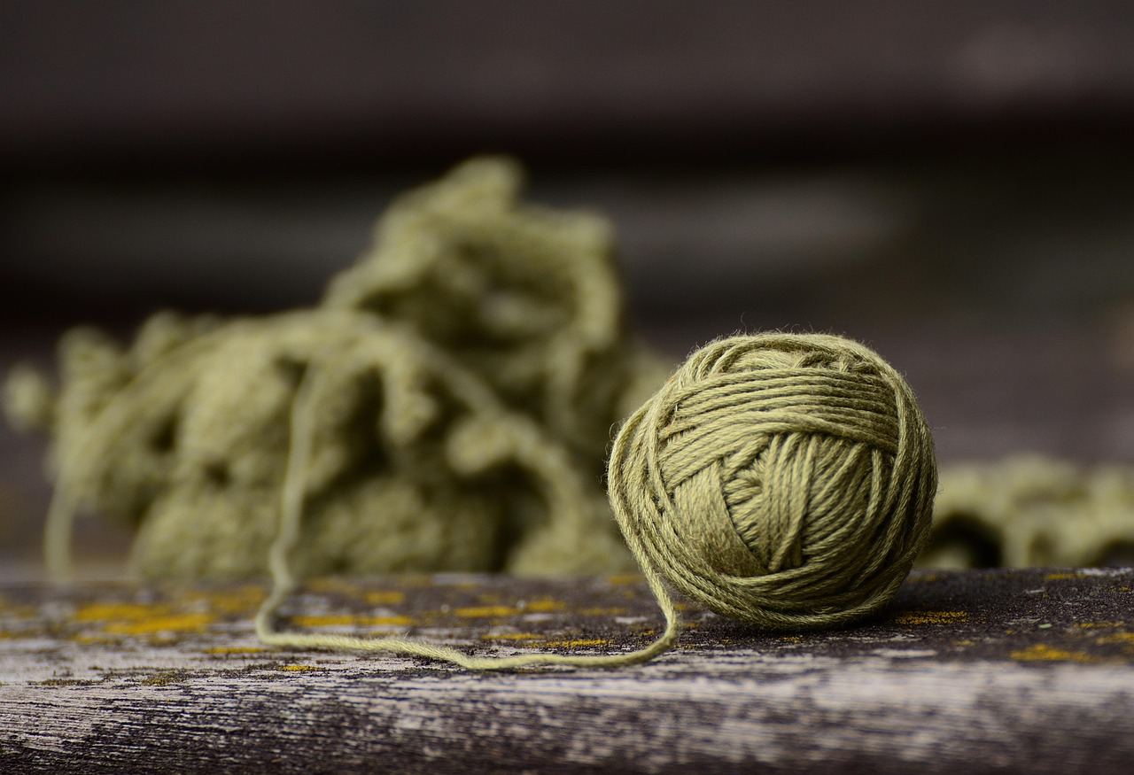 A ball of olive green yarn sits on a wooden surface, perfect for crochet projects. Is Crochet for you? Let's find out!