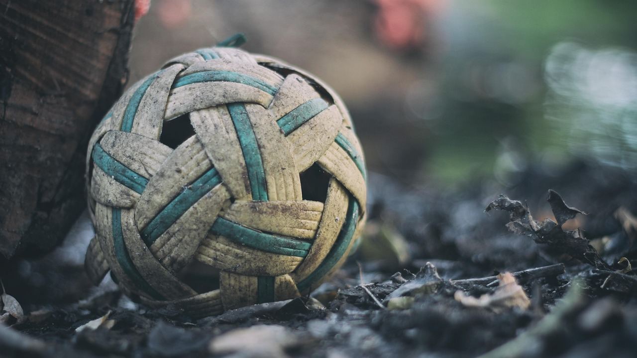 A vibrant sepak takraw ball, intricately woven from rattan, resting on a wooden court surface.