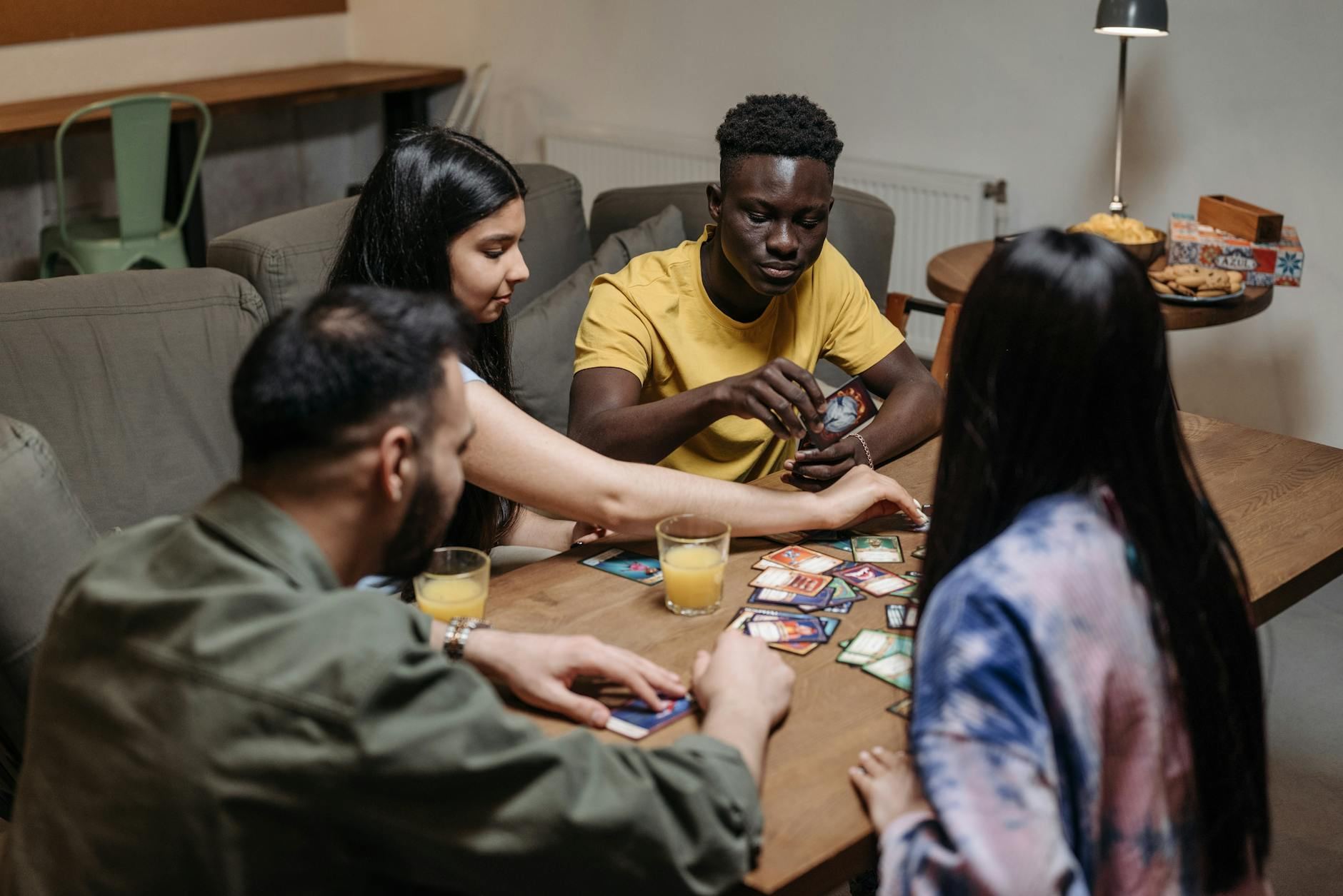 A diverse group of friends playing a strategic card game while enjoying drinks indoors.