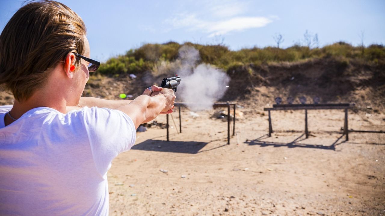A close-up of a sleek, modern pistol resting on a shooting range table, surrounded by ear protection and ammunition.