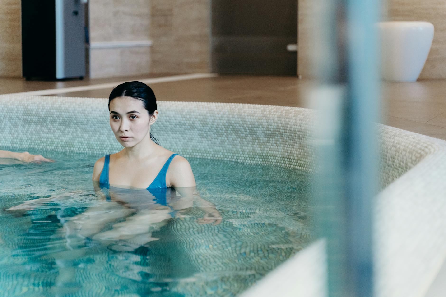 A serene woman relaxes in a tranquil indoor swimming pool, embodying wellness and leisure.