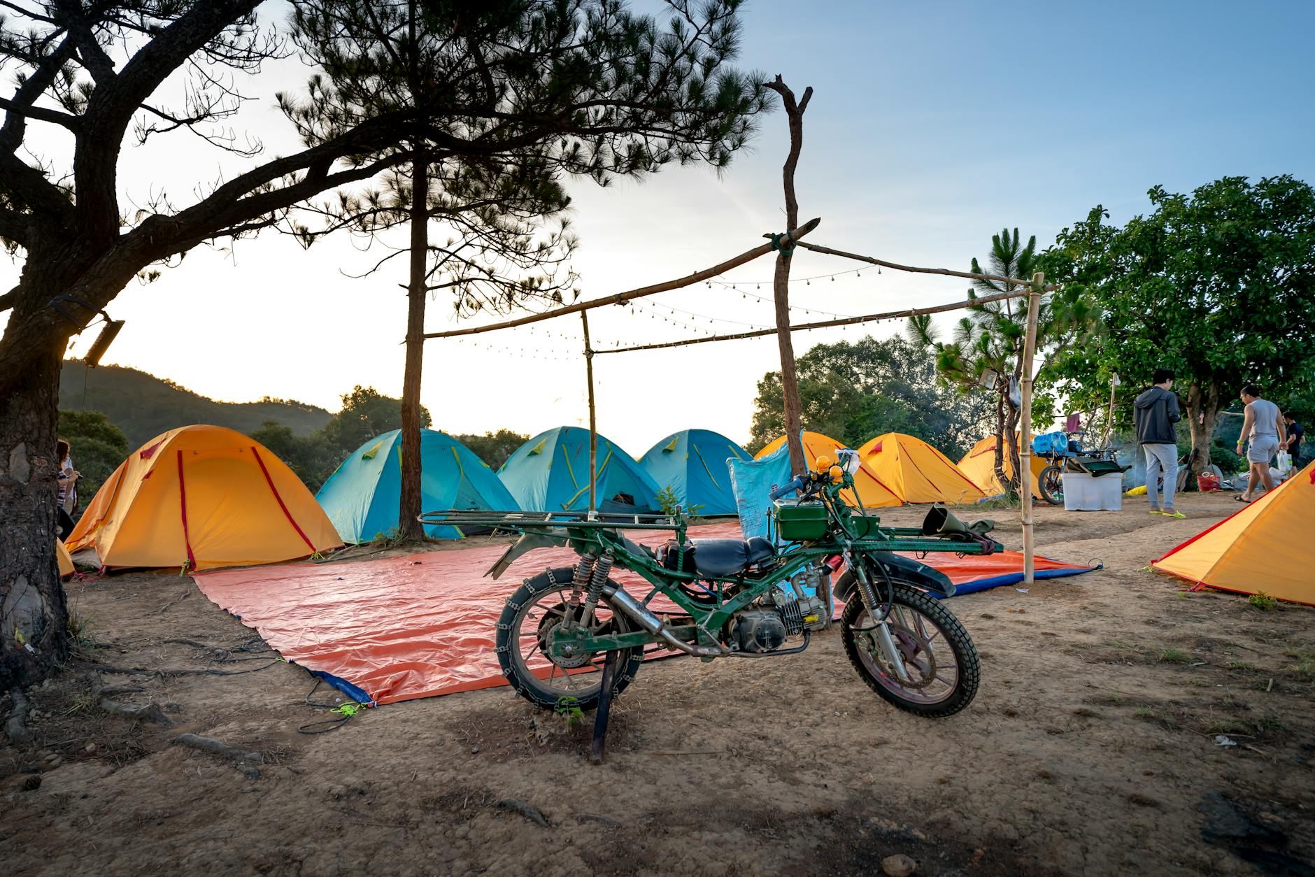 Scenic campsite with colorful tents and a vintage motorcycle parked in a tranquil setting.